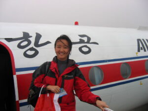 Woman in red coat stands in front of a Koryo airlines airplane